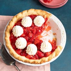 a strawberry pie with whipped cream on top sits on a table next to plates and utensils