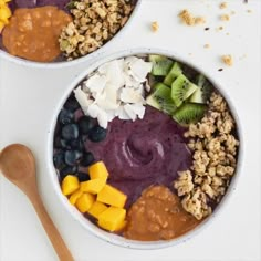 two bowls filled with fruit, nuts and granola on top of a white table