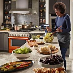 a woman standing in front of a counter filled with plates and bowls full of food