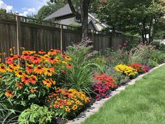 colorful flowers line the side of a fenced in garden area on a sunny day