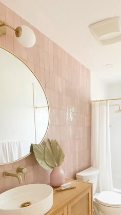 a bathroom with pink tiles and white fixtures, including a round mirror above the sink