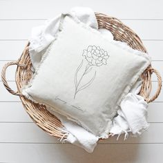 a white pillow with a flower drawn on it sitting in a wicker basket next to some folded towels