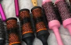 several different types of hair brushes lined up on a white surface with pink and black handles