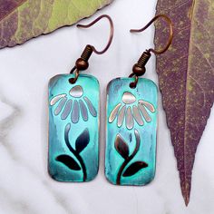 a pair of earrings with flowers painted on them are sitting next to a green leaf