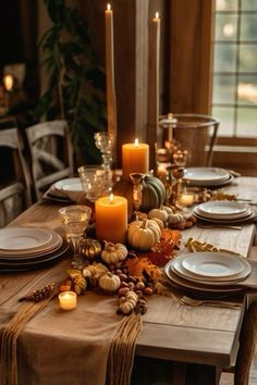 a table with candles, plates and pumpkins is set for an elegant thanksgiving dinner