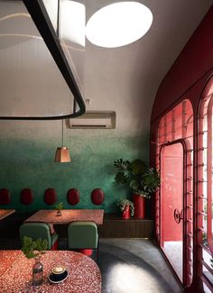 the interior of a restaurant with green and red walls, round tables, and potted plants