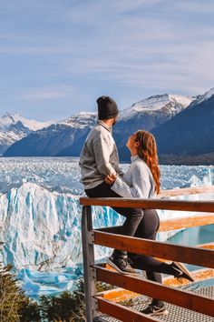 a man and woman sitting on a bench looking at the glacier in front of them