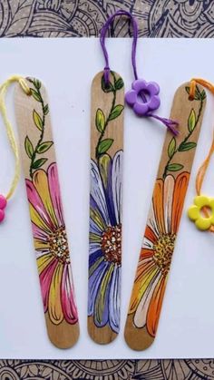 three wooden bookmarks with flowers painted on them and some beads attached to the handles