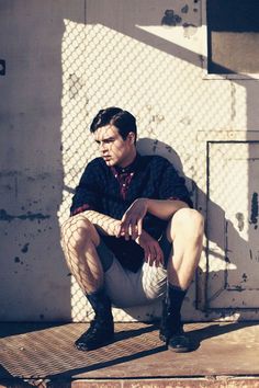 a man sitting on top of a wooden platform next to a building with a chain link fence