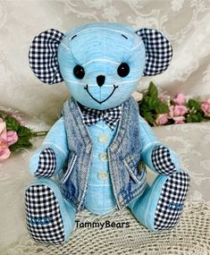 a blue teddy bear sitting on top of a white cloth covered table next to pink flowers