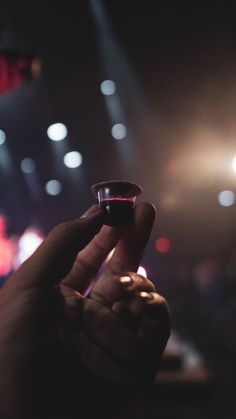 a hand holding a small object in front of a stage with lights on the ceiling