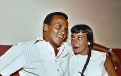 a man and woman are sitting on a red couch posing for the camera with their arms around each other