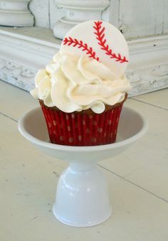 a cupcake with white frosting and a baseball on top is sitting in a pedestal