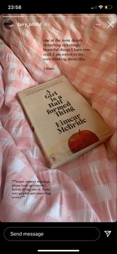 a book is laying on top of a pink comforter that has an apple on it