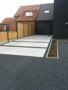 an empty driveway in front of a house with a wooden fence and black garage doors