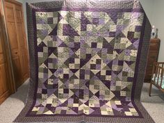 a large purple and green quilt on display in a room next to a crib