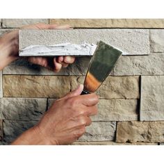 two hands are holding a brick wall with a trowel in front of it