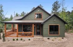 a small green house in the woods with wood trimmings on the front porch