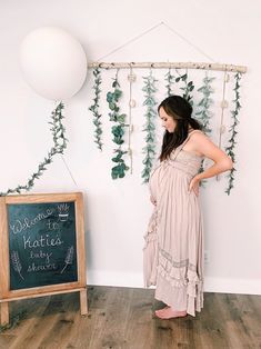 a woman standing in front of a chalkboard with greenery on it and a white balloon