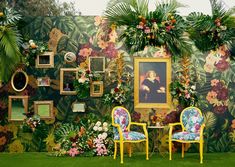 two chairs and a table in front of a wall with flowers, plants and pictures on it