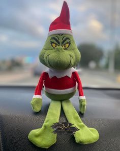 a green stuffed toy sitting on top of a car dashboard with an evil grin face