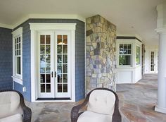 two wicker chairs sitting in front of a stone wall on a porch with glass doors