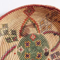 a close up of a woven basket on a white surface with red, green, yellow and orange designs