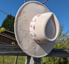 This truly one-of-a-kind fedora hat is perfect to add a special touch to your outfit or hang as a unique floral wall decoration. It's burned entirely by hand using a pyrography tool with an original and entirely freehanded design (never using a stencil or laser machine.) The beige material burns a delicate warm tan. This design features detailed magnolia flowers burned upon the top brim. Lastly, this fedora is adorned with a floral print hat band for a feminine look. Brim is roughly 4 inches wid Country Style Brimmed Fedora For Spring, Spring Country Style Brimmed Fedora, Country Style Spring Fedora With Brim, Handmade Pink Fedora For Spring, Adjustable Felt Hat For Spring Country Events, Spring Country Event Hat Band With Short Brim, Adjustable Felt Bucket Hat For Spring, Short Brim Felt Hat For Country Events In Spring, Flat Brim Felt Hat For Country Events In Spring