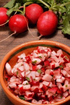 radishes are in a bowl on a table next to greens and other vegetables