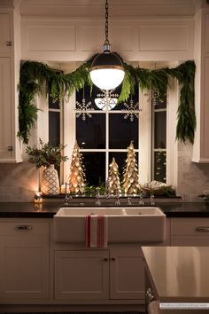 a kitchen decorated for christmas with evergreen garland and pine cones on the window sill