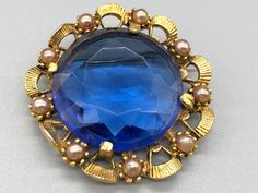 A beautiful vintage blue brooch with a faux pearl border. Approximate measurements  Length - 4.5 cm Width - 4.5 cm  * Due to this item being vintage there may be markings on the piece.  Please view the video and photos to see the condition of the jewellery. Blue Costume Jewelry Brooch For Wedding, Blue Victorian Brooch For Formal Occasions, Blue Victorian Brooches For Formal Occasions, Victorian Blue Brooch For Formal Occasions, Blue Round Brooch For Formal Occasions, Formal Blue Round Brooch, Formal Blue Round Brooches, Vintage Blue Brooch Pin, Crystal Brooch