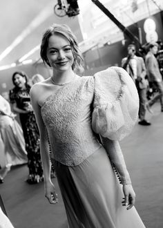 a black and white photo of a woman in a dress smiling at the camera, with other people around her