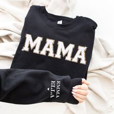 "This cozy crewneck is the perfect gift for a Mama ( or for yourself of course)!  Featuring the word \"Mama\" in bold letters on the front, stylish and cute all year wear. The shirt comes personalized with her kids names on the sleeve. The chenille letter patches are a beautiful white chenille with gold glitter backing, exuding an aura of confidence and vibrancy that's bound to catch everyone's eye. What sets them apart is the sumptuous, fluffy chenille texture that's not only pleasing to the touch but also adds an extra dimension of texture to your outfit. To add a touch of glitz and glamour to your day-to-day look, each chenille letter patch is backed with a gold glitter. This subtle yet enchanting detail adds a dash of sparkle to this cozy sweatshirt. 𝐇𝐎𝐖 𝐓𝐎 𝐎𝐑𝐃𝐄𝐑 1. Select th Black Crew Neck Top With Letter Embroidery, Fall Crew Neck T-shirt With Name Print, Embroidered Crew Neck Tops For Gifts, Black Long Sleeve Top As Gift, Black Long Sleeve Top As A Gift, Long Sleeve Tops With Embroidered Text For Gift, Black Crew Top With Letter Embroidery, Crew Neck Top With Embroidered Text As Gift, Fall Tops With Embroidered Graphics For Gift