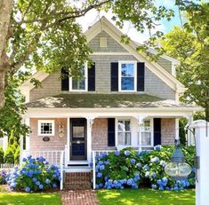 a white house with blue flowers in the front yard