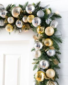 a christmas wreath with gold and silver ornaments hanging on the side of a white door