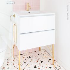 a bathroom with pink tiles and gold fixtures on the floor, including a white sink