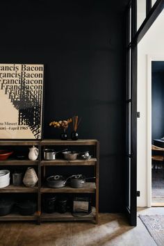 a room with black walls and wooden shelves filled with pots, pans and other items