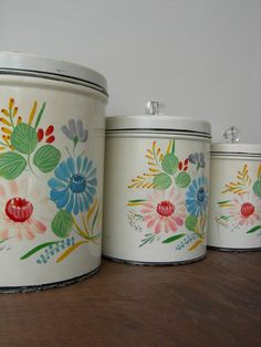 three canisters with flowers painted on them sitting on a wooden table next to a wall