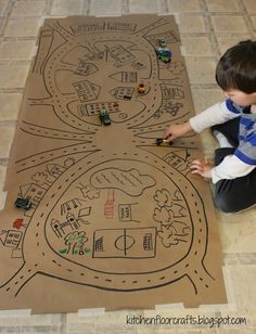 a young boy sitting on the floor playing with a cardboard map that has cars and roads drawn on it