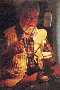 an old man sitting at a table working on some kind of crafting project with scissors and thread