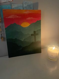 a lit candle sitting next to a painting on a wall with mountains in the background