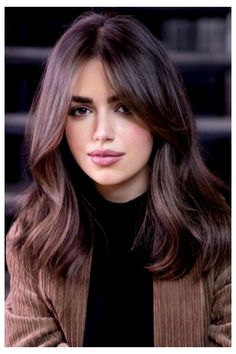 a woman with long brown hair sitting in front of some stairs and looking at the camera