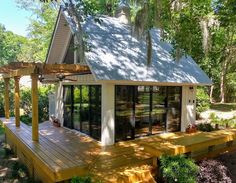 a small white house sitting on top of a wooden deck next to a lush green forest