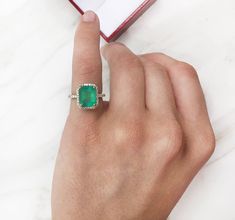 a woman's hand holding an emerald and diamond ring in front of a book