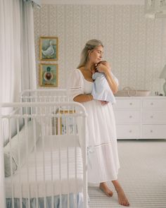 a woman holding a baby in her arms while standing next to a white crib