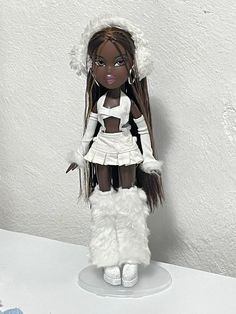 a doll with long hair and white clothes sitting on top of a table next to a wall