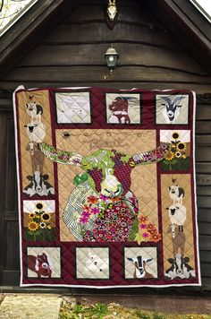 a quilt hanging from the side of a building with animals and flowers on it's front