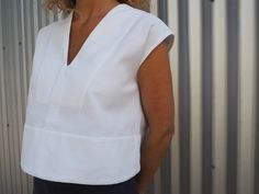 a woman standing in front of a metal wall wearing a white shirt and black pants