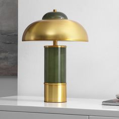 a green and gold lamp sitting on top of a white table next to a book