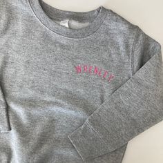 Choose from heather grey, navy, pink, black or royal, granite grey or white. Each sweatshirt is made from 60% cotton and 40% polyester. Each sweatshirt is embroidered with curved name in a small block font.  Please wash on cold and dry on low. If you are wanting a different design, more wording, or a different clothing style, please send me a message so we can discuss the details. In the notes to seller please enter the name/wording exactly how you would like it to read Click this link for white custom organic cotton t-shirts:  https://www.etsy.com/listing/988105502/organic-cotton-custom-name-embroidered?ref=shop_home_feat_1&pro=1&frs=1 If you need this order rushed, please add one of these  to your cart: Rush my order https://www.etsy.com/listing/1043569716/rush-my-order-for-t-shirts?ref= Heather Grey Embroidered Logo Sweatshirt For Winter, Heather Grey Winter Sweatshirt With Embroidered Logo, Winter Heather Grey Sweatshirt With Embroidered Logo, Gray Long Sleeve Sweatshirt With Letter Embroidery, Gray Long Sleeve Top With Letter Embroidery, Gray Winter Sweatshirt With Embroidered Text, Gray Long Sleeve Top With Embroidered Text, Gray Embroidered Winter Tops, Monogram Sweater